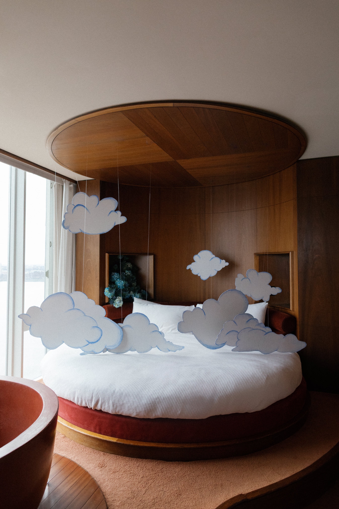 Cardboard clouds hanging by string above a round bed in a hotel suite