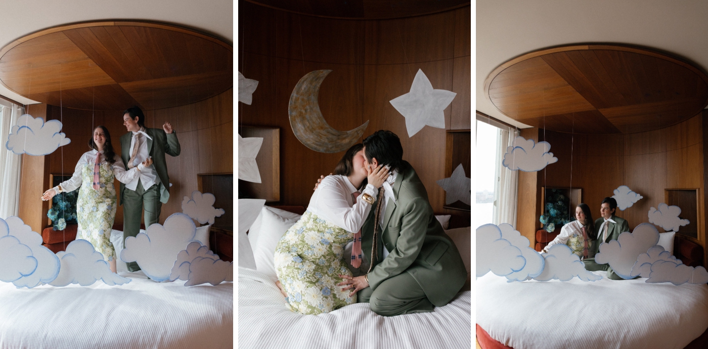 Two women jump on a round hotel bed that is surrounded by cardboard clouds